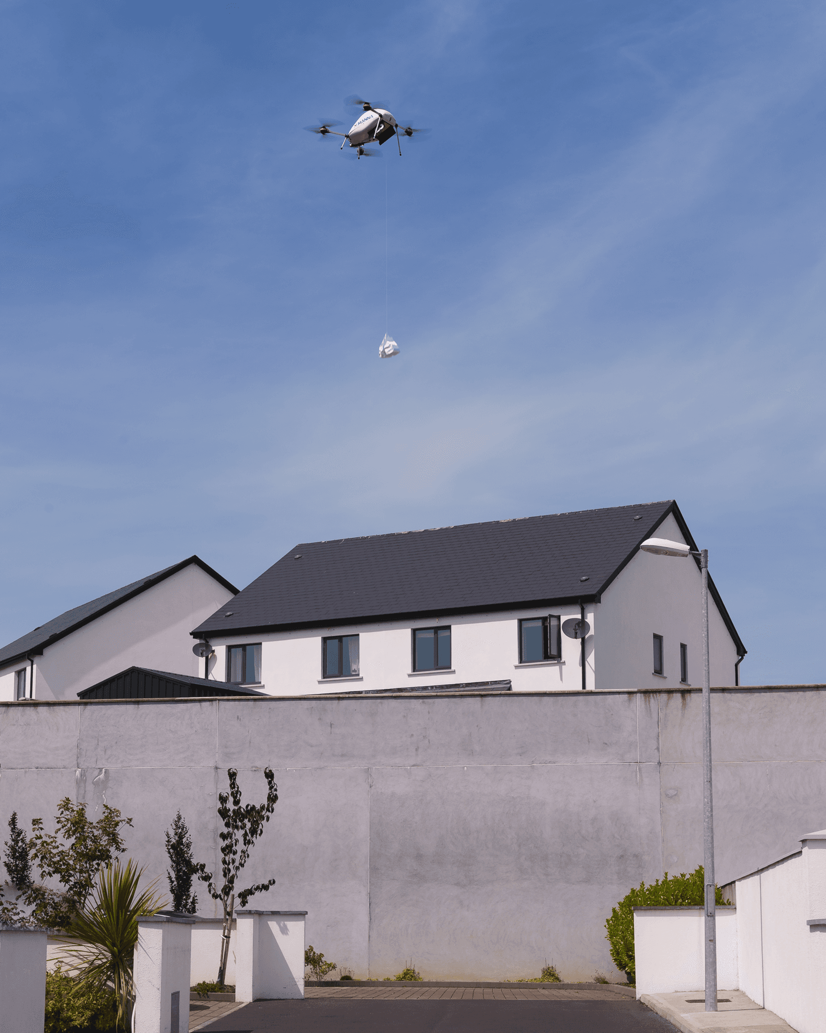 A Manna aircraft lowering an order on a tether above a house